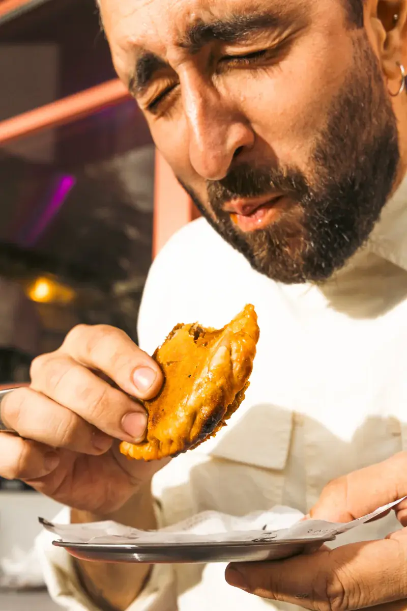 Cliente mordiendo una empanada recién servida en el mostrador del local